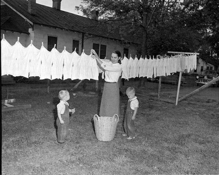 Moments quotidiens intemporels captures en photos historiques - #31 Sur cette image de 1955, une femme accroche son linge sur une corde à linge dans son jardin. En grandissant dans les années 1960 et 1970, chaque jardin de ma rue avait une corde à linge et les voisins se criaient des nouvelles tout en étendant leur linge