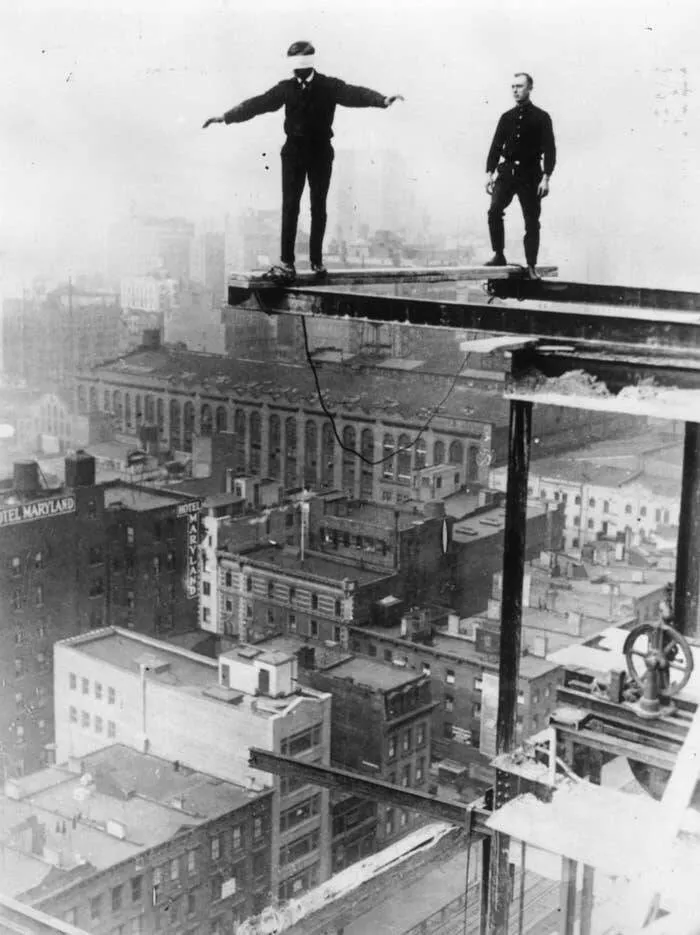 Images fascinantes de chantiers historiques - #1 Un ouvrier du bâtiment américain marche les yeux bandés sur une poutre de construction, perché à vingt étages de hauteur dans la ville de New York.