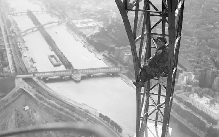 Images fascinantes de chantiers historiques - #24 Un ouvrier engagé pour repeindre la massive Tour Eiffel est photographié assis en hauteur sur une section de la tour, avec un seau de peinture attaché à sa ceinture. Images fascinantes de chantiers historiques - #24 Un ouvrier engagé pour repeindre la massive Tour Eiffel est photographié assis en hauteur sur une section de la tour, avec un seau de peinture attaché à sa ceinture.