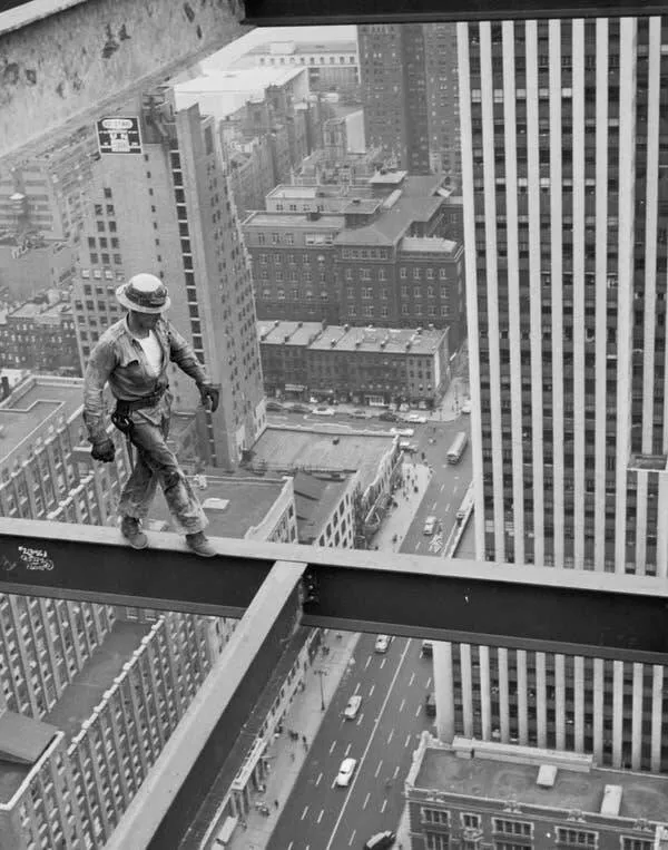 Images fascinantes de chantiers historiques - #4 Un ouvrier de construction déambule sur une poutre, haut au-dessus des rues de la ville.